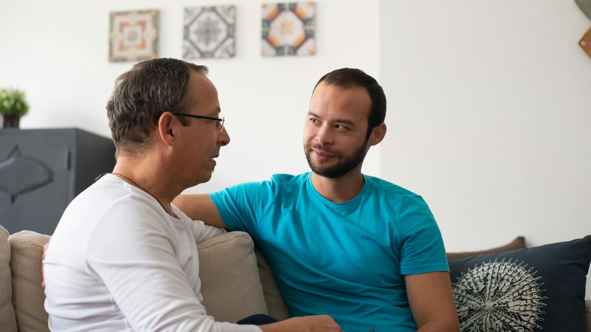 Two men share a heartfelt conversation on a cozy sofa in a modern living room.
