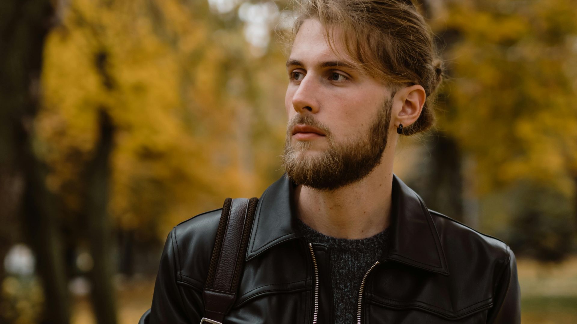Young man with a beard in a leather jacket outdoors during autumn.