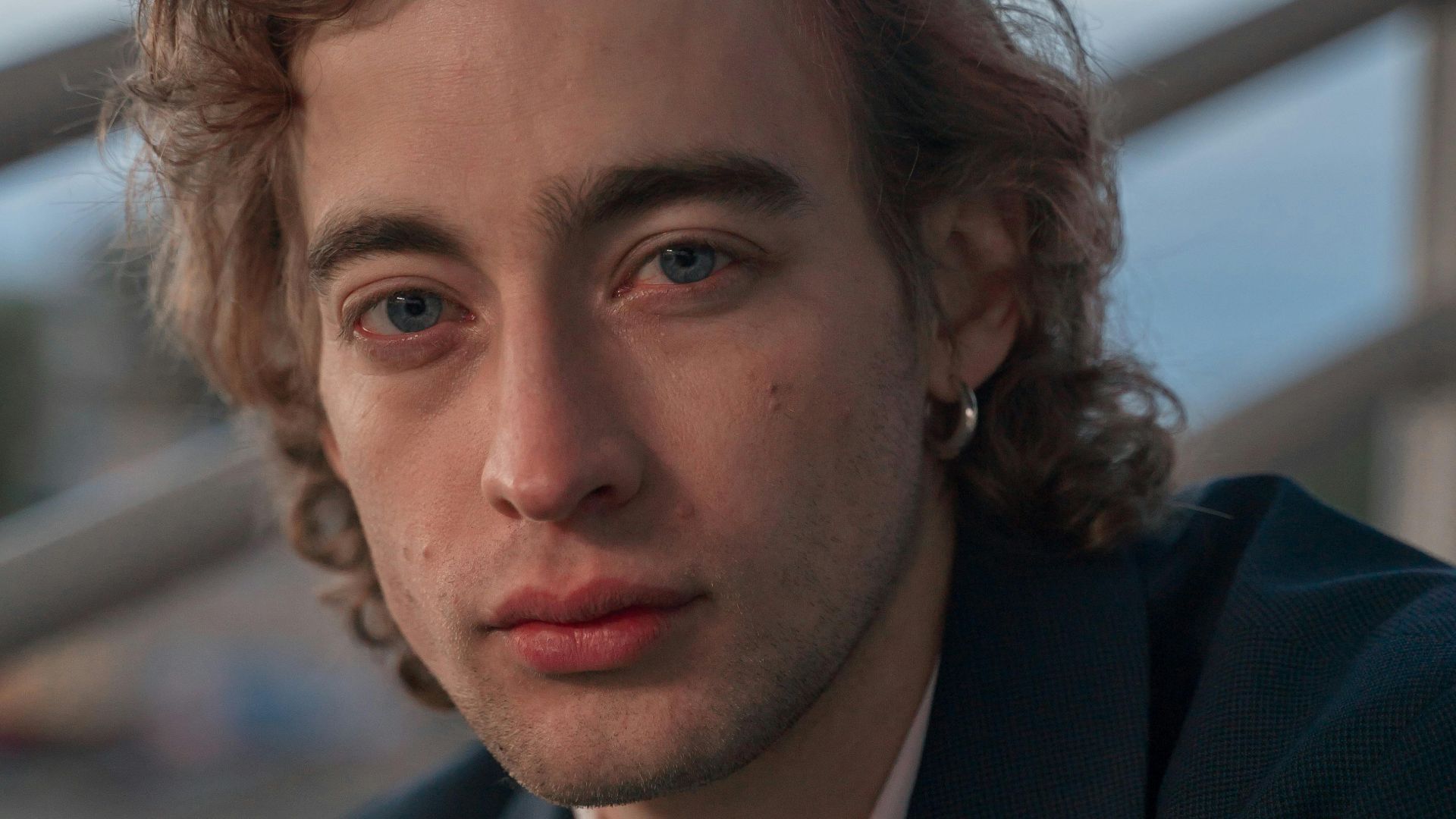 Portrait of a young man with curly hair wearing a suit jacket, exuding a thoughtful expression.