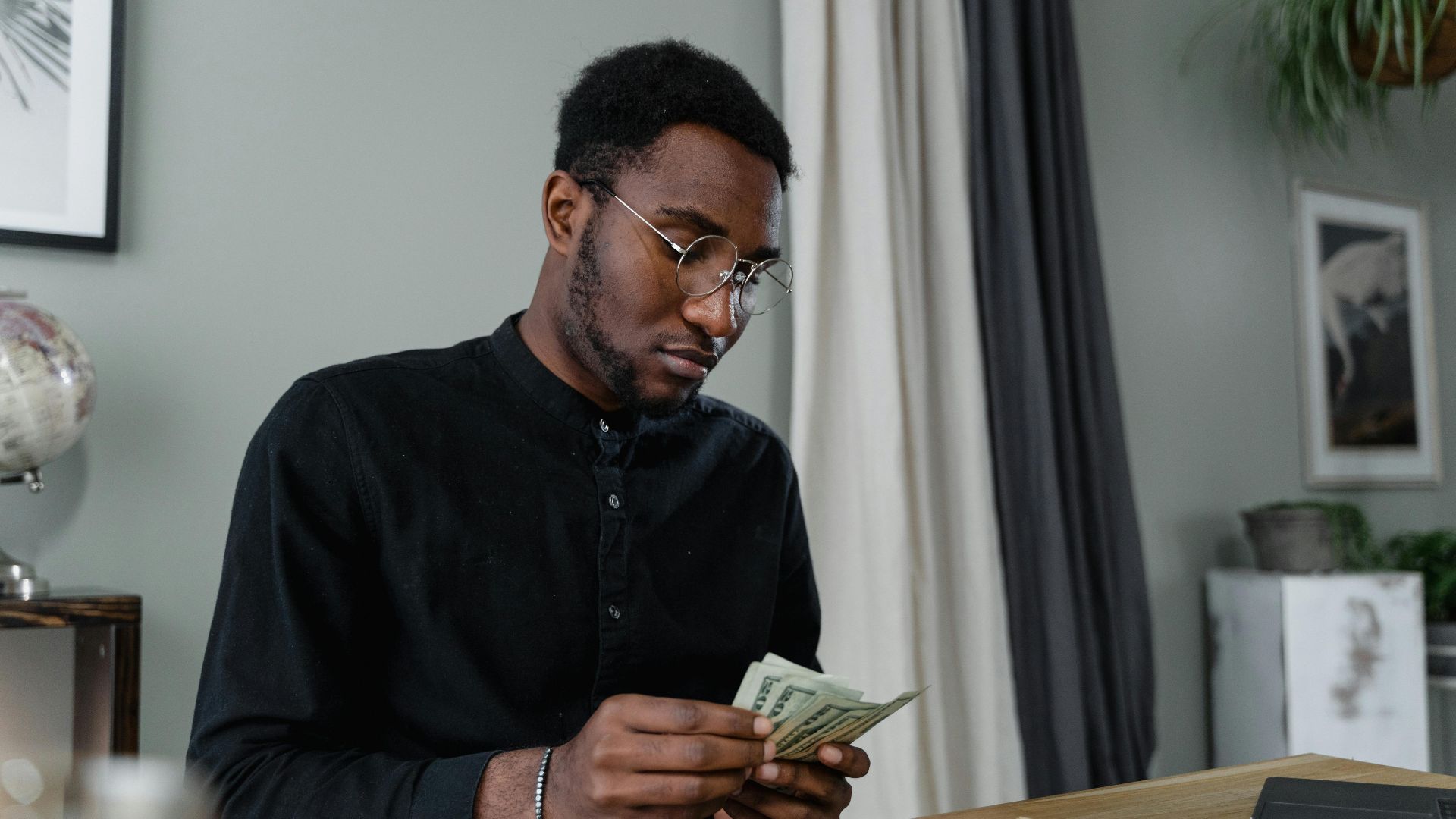 A focused man in glasses counting cash at a desk, indicating financial management.