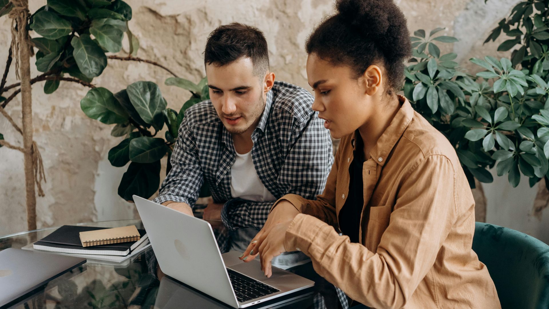 Two colleagues working together on a laptop in a modern office setting.