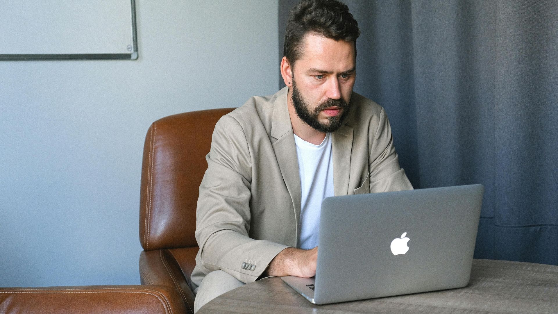 Concentrated bearded male entrepreneur wearing formal suit browsing netbook while working on startup