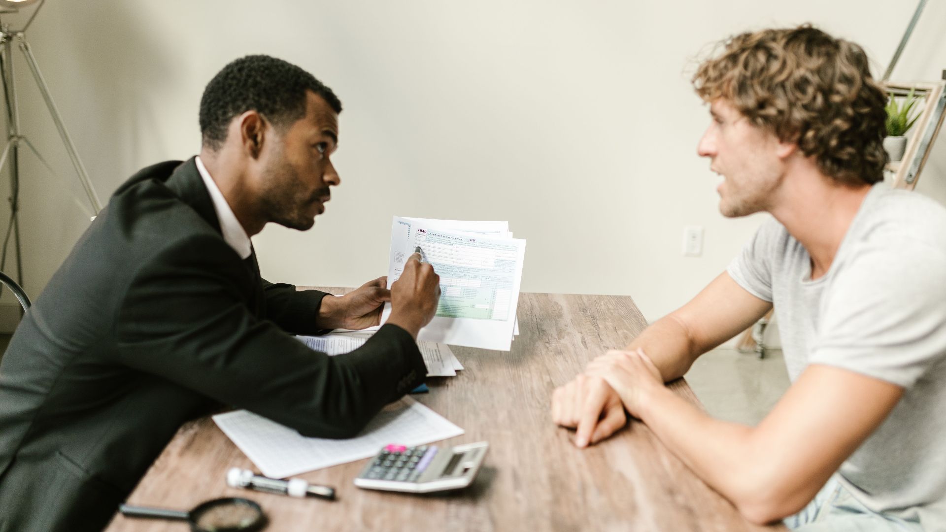 A financial advisor discusses paperwork with a client at a desk in a modern office.