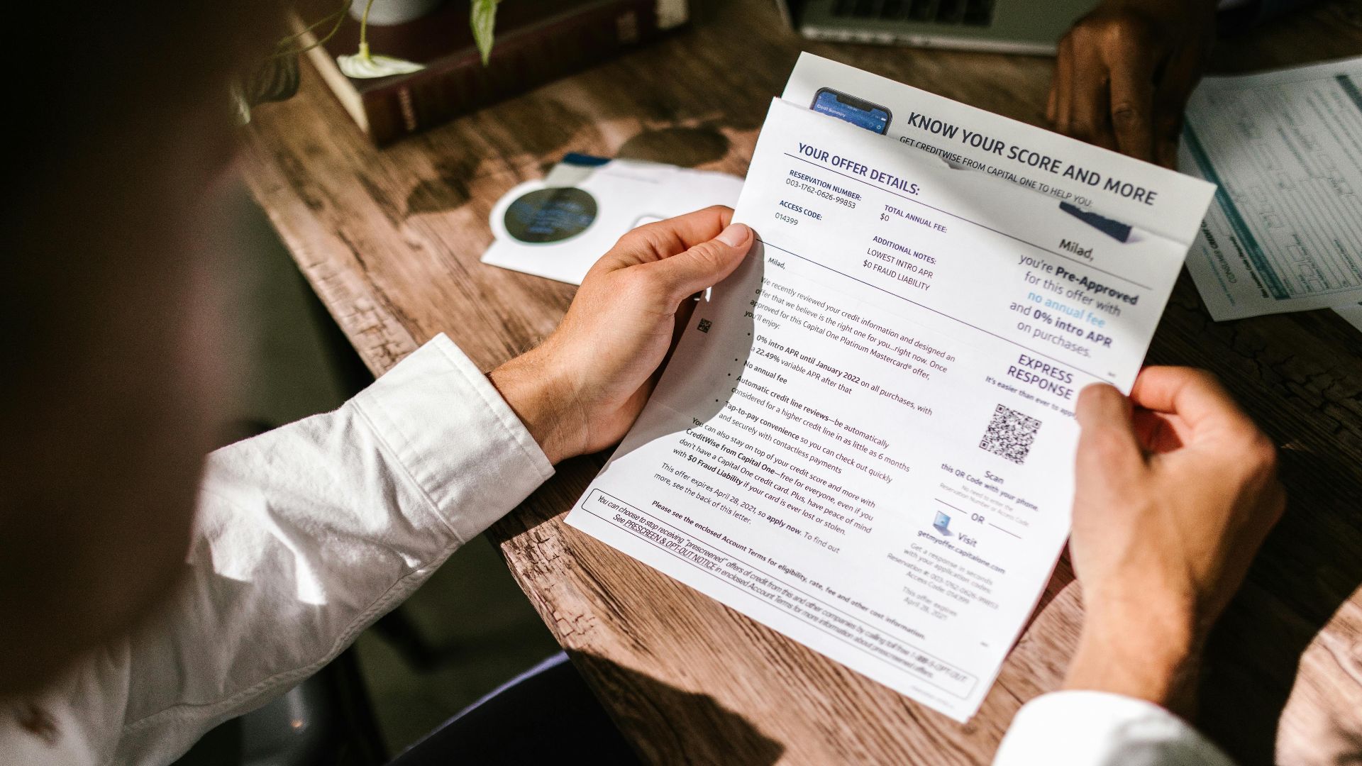 An adult man examining a financial document under natural light at a wooden desk, emphasizing finance and reading.
