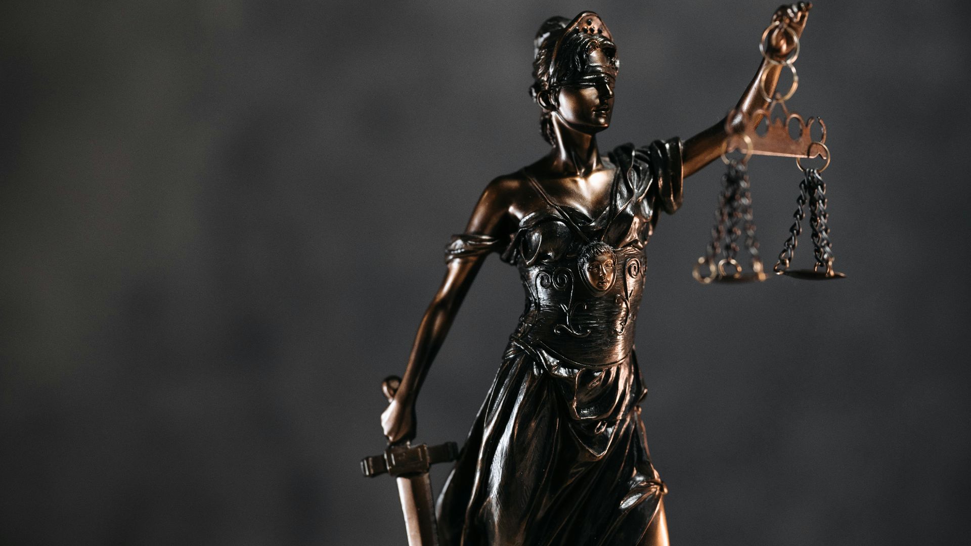 Detailed bronze Lady Justice statue with scales and sword against a dark background, symbolizing law and justice.