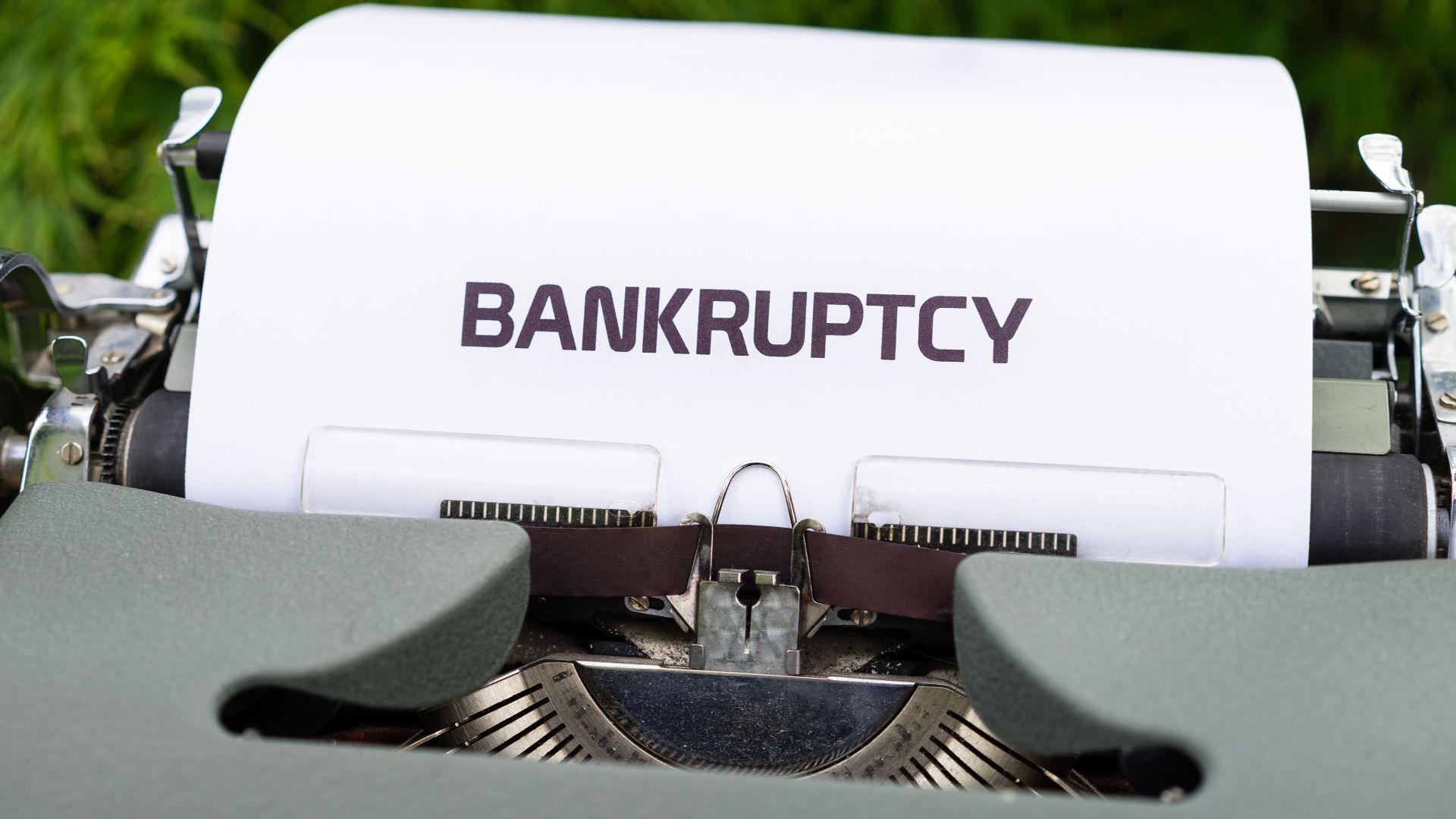Close-up of a typewriter with the word 'BANKRUPTCY' on paper, surrounded by greenery.