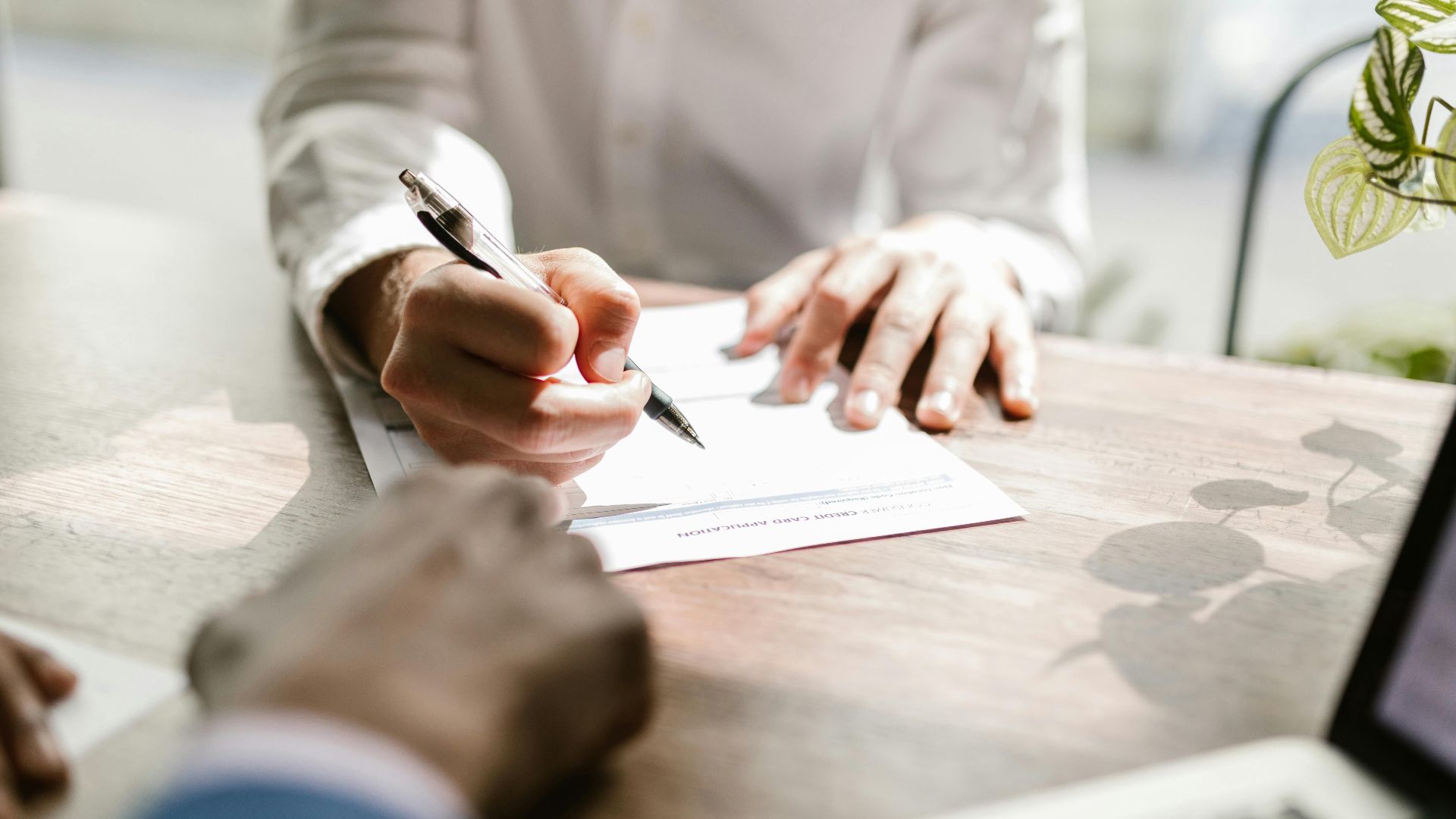 Close-up of people signing a document at a desk, highlighting professional business interaction.