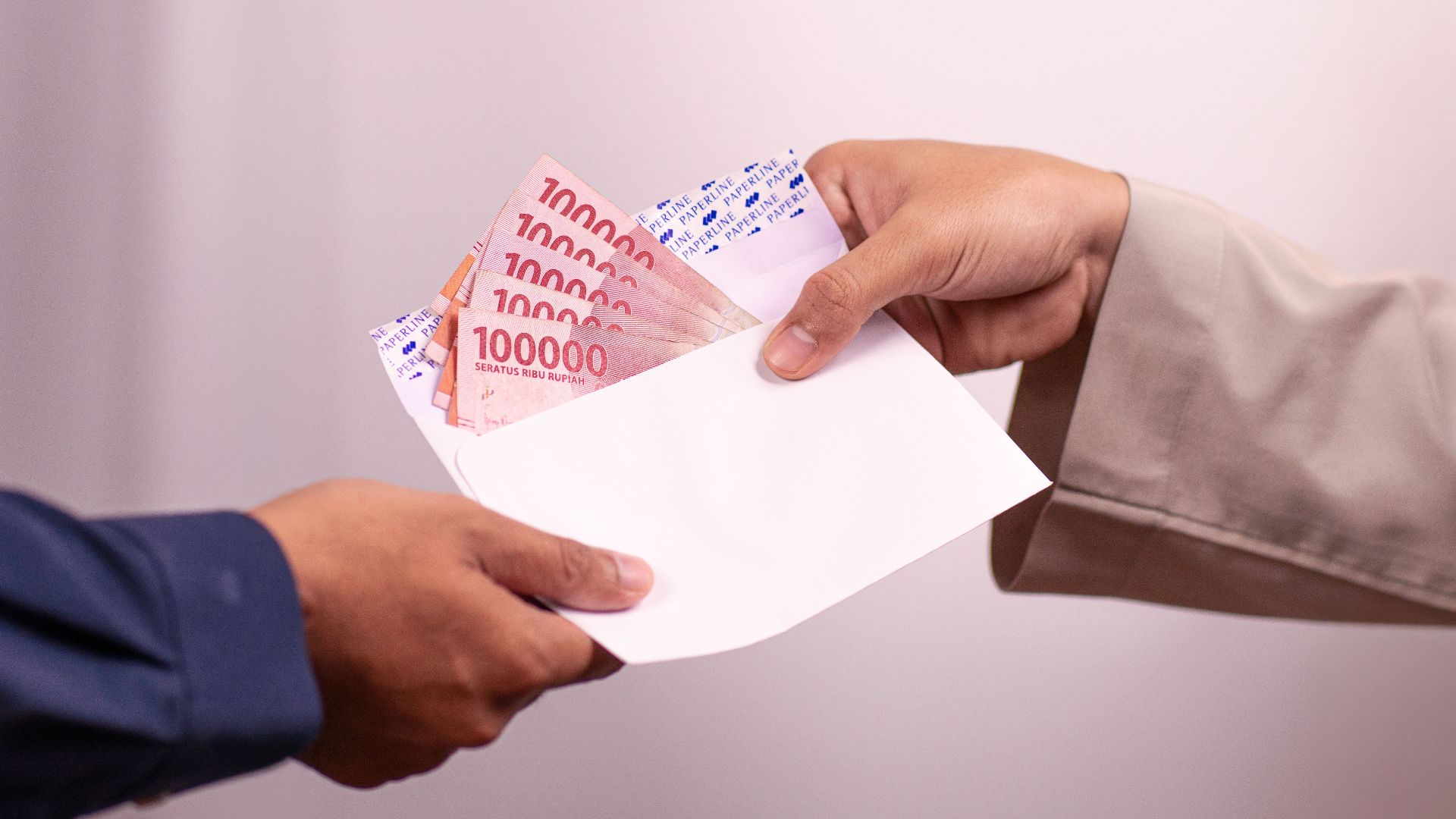 Hands giving and receiving Indonesian rupiah in an envelope, symbolizing financial transaction.