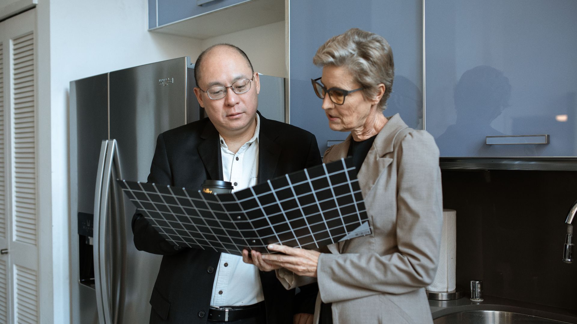 Two business professionals review documents in a modern office kitchen setting.