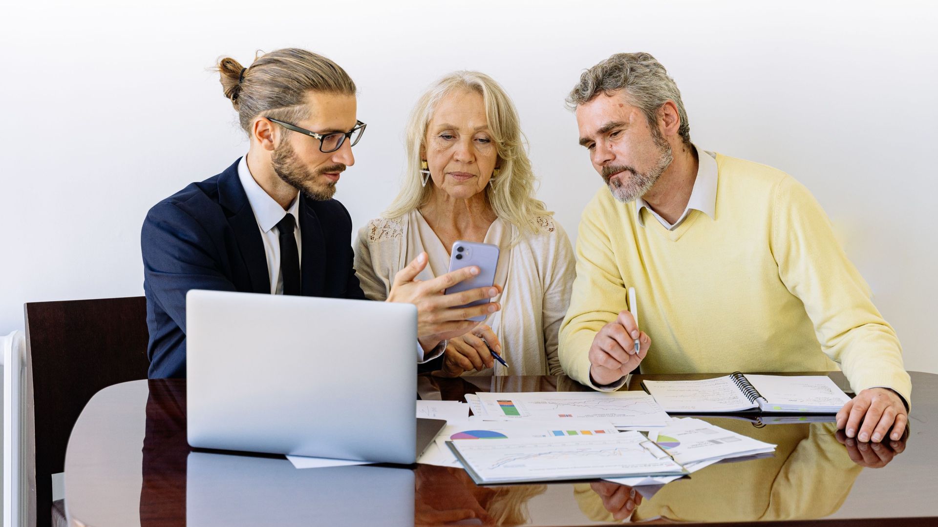 Three individuals collaborating on financial documents during a business meeting.