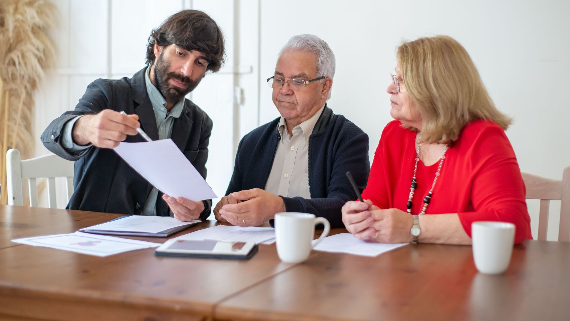 Elderly couple discussing documents with advisor at a wooden table indoors.