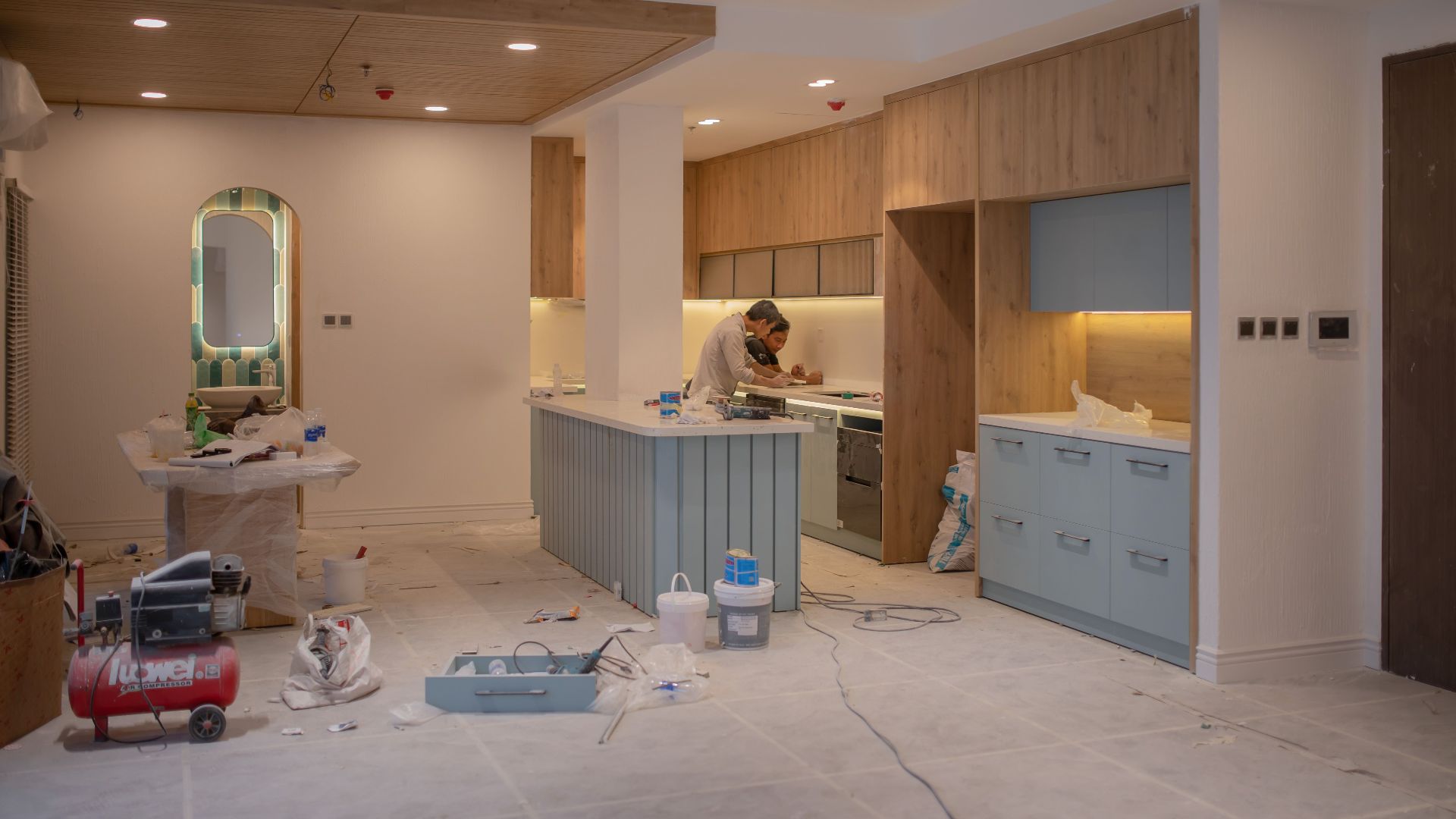 A modern kitchen undergoing renovation, featuring a worker, tools, and materials.