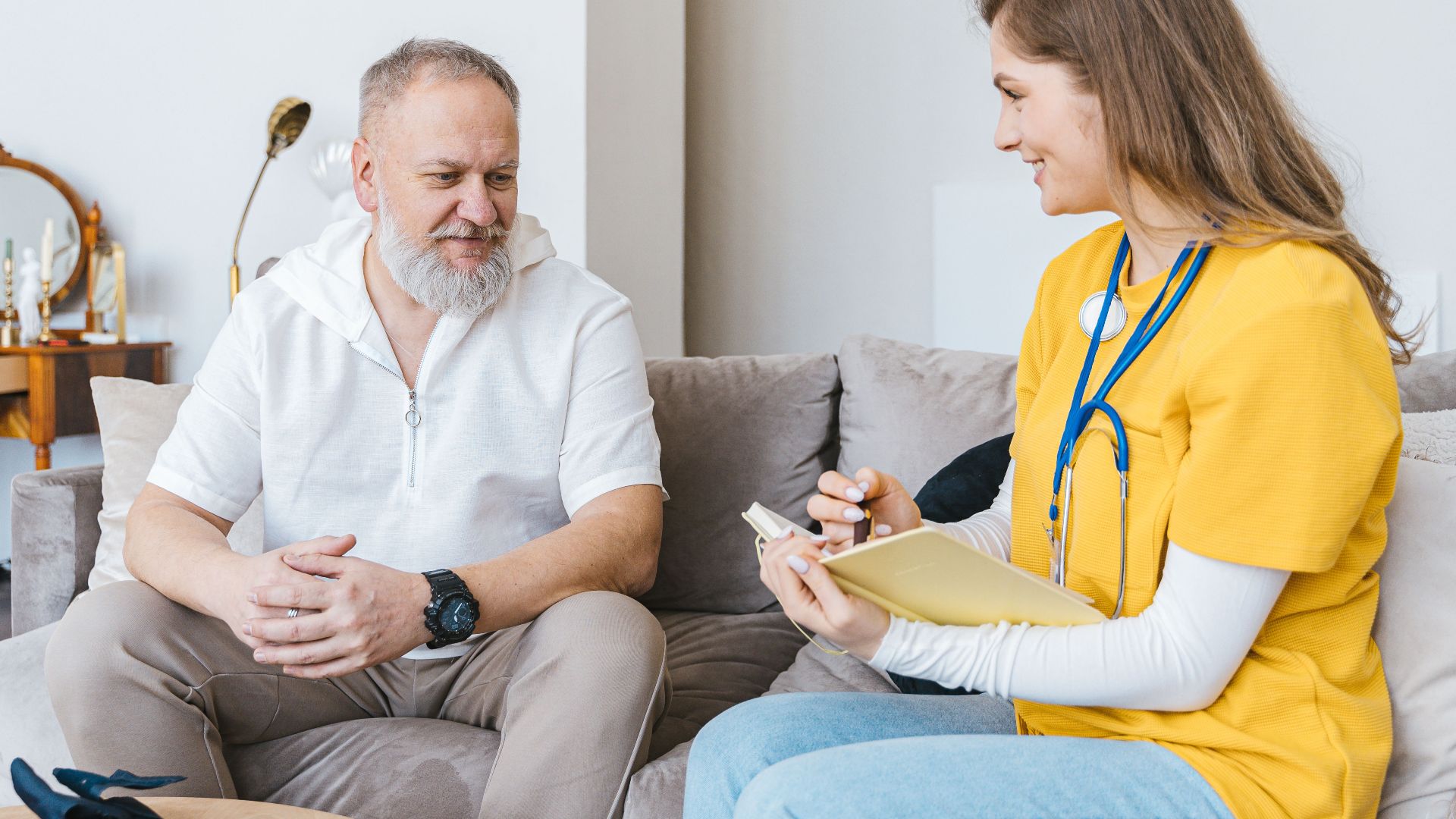 A healthcare professional smiles while consulting with an elderly man in a cozy indoor setting.