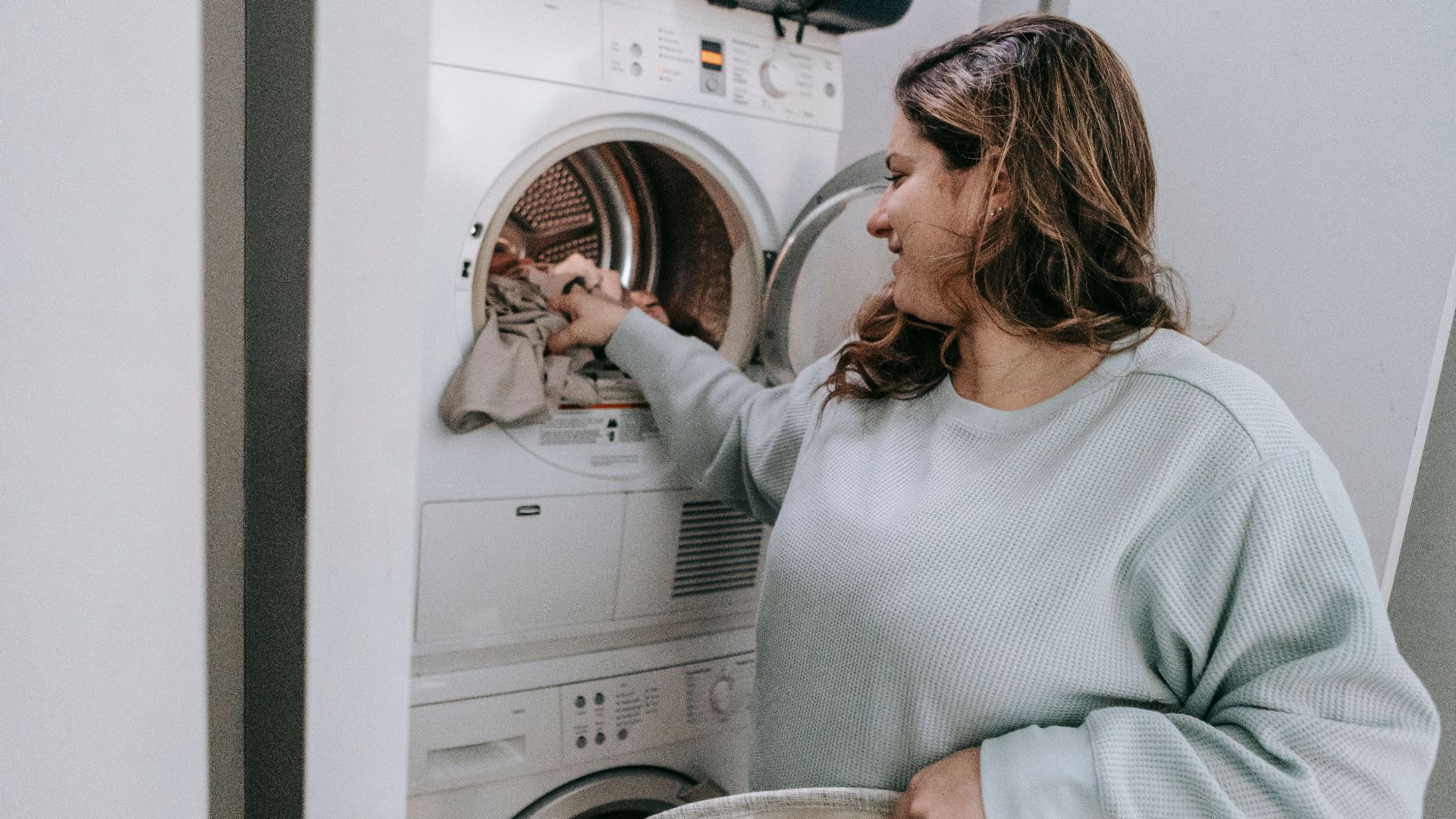 Glad female in casual wear loading dirt clothes in modern white washing machine while sitting in bathroom during household routine