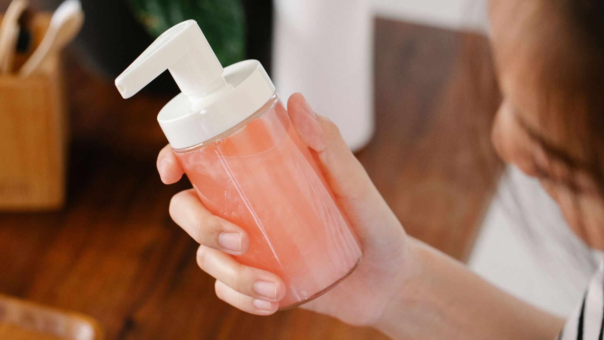 From above crop anonymous dark haired female standing with soap dispenser in hand