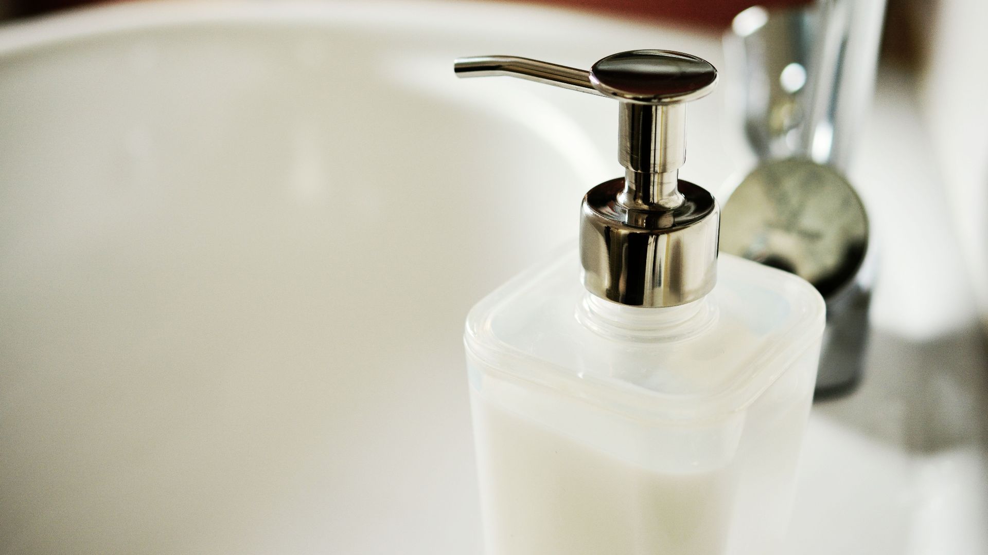 Close-up of a modern soap dispenser beside a sink in a clean bathroom.