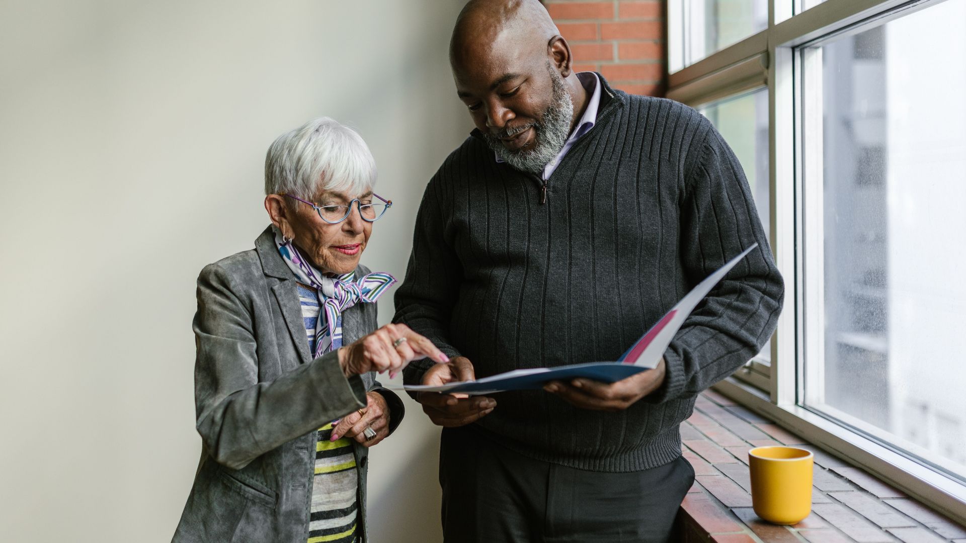 An elderly man and woman engage in a business discussion, reviewing documents in an office setting.