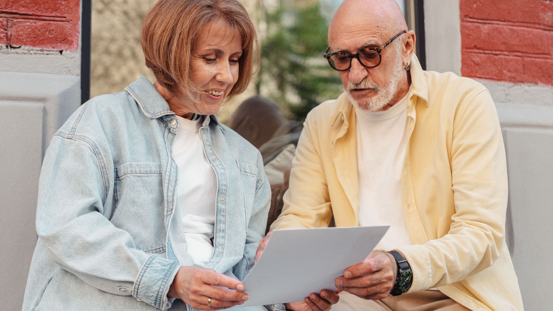 Elderly couple reading a document together while sitting outside at a cafe.