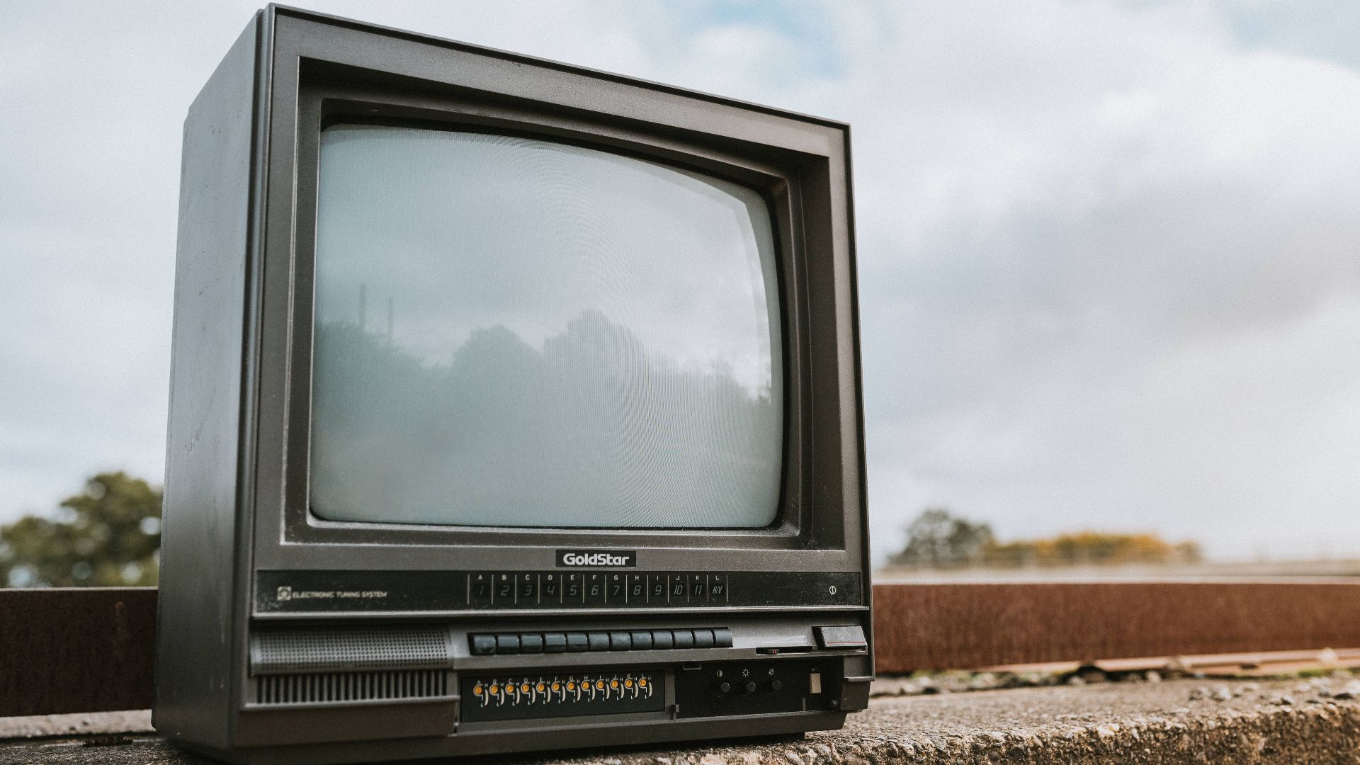 Black old fashioned obsolete television with reflection on screen placed on concrete railing against cloudy ski on street on blurred background