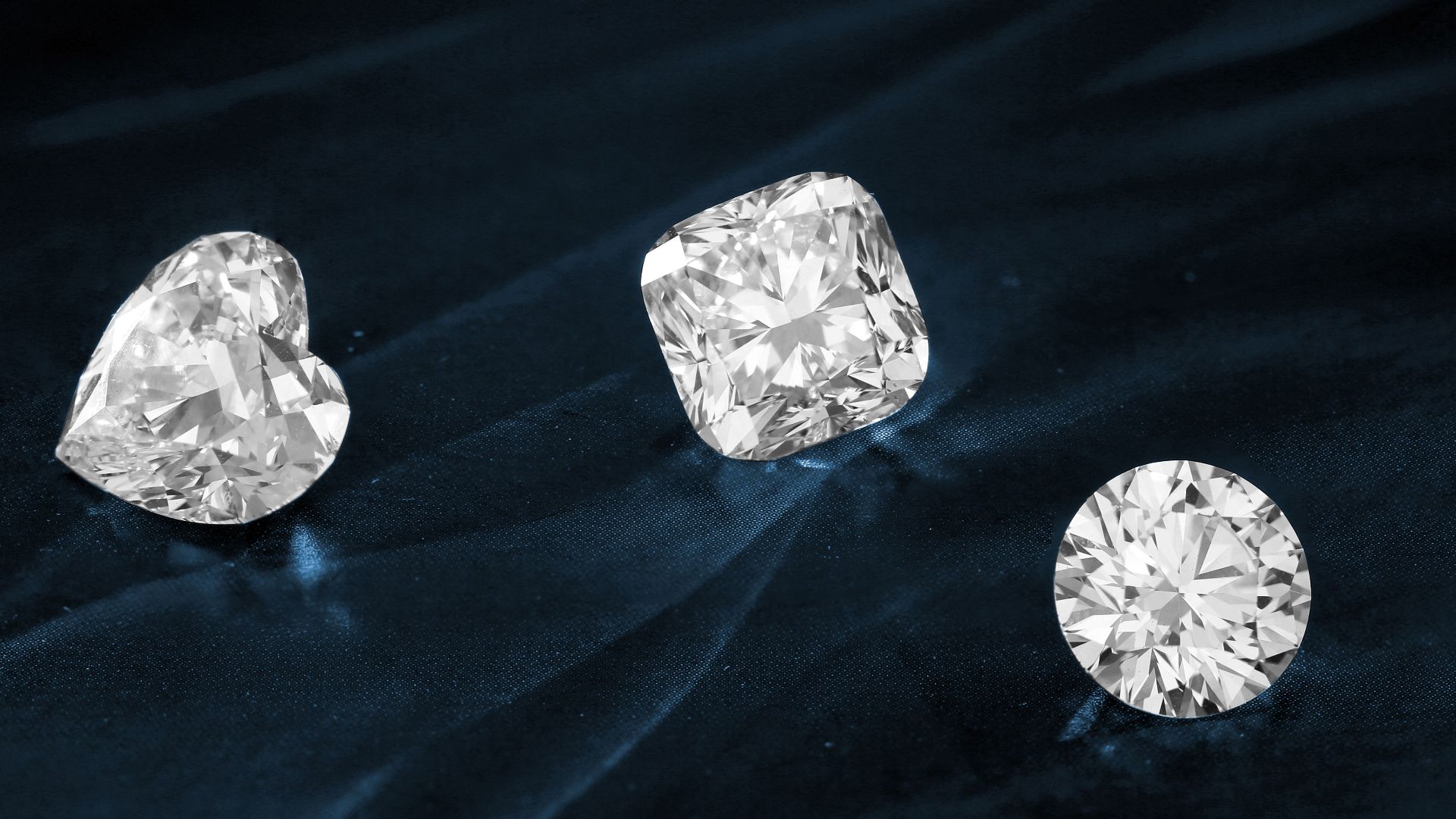 Three exquisite diamonds featuring heart, cushion, and round cuts displayed on dark fabric.