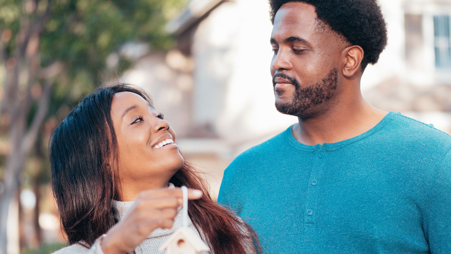 Smiling couple holding a small house model, symbolizing new home ownership celebration.