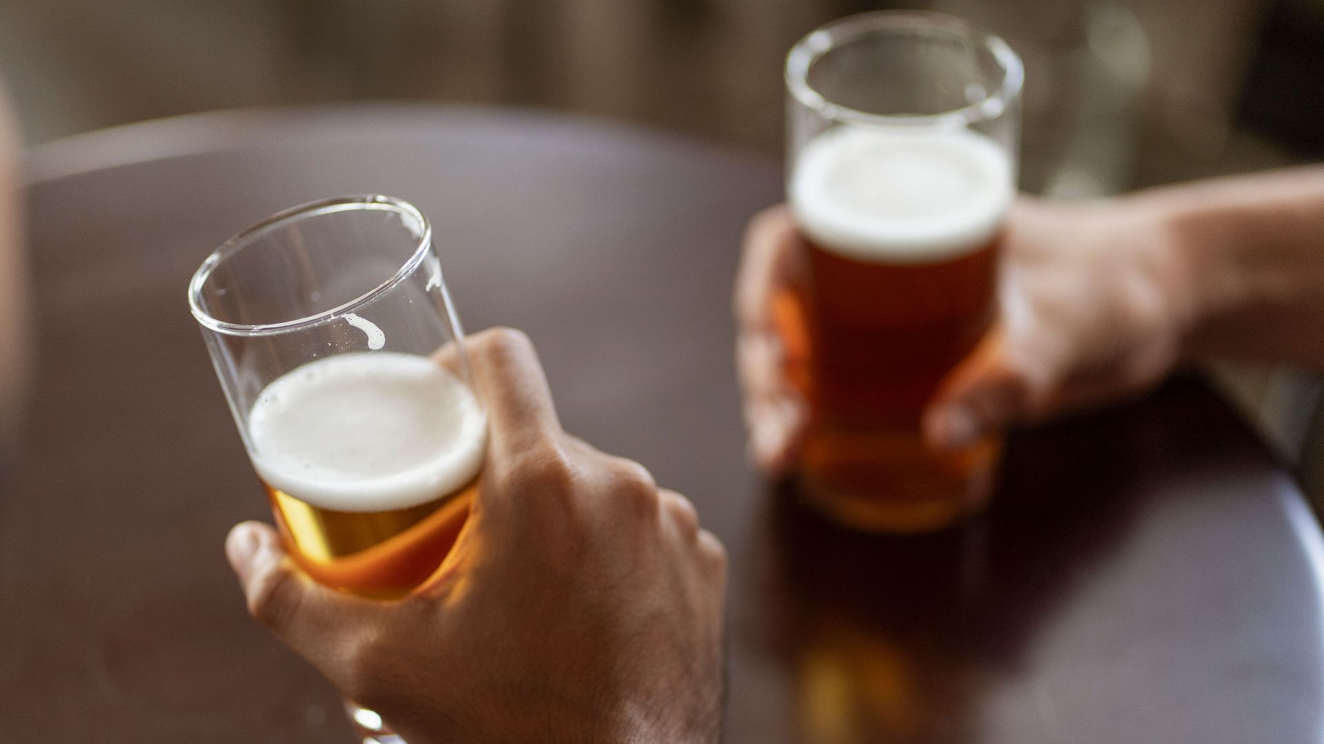 Two individuals enjoying alcoholic beverages in a casual setting, focus on hands and beer glasses.