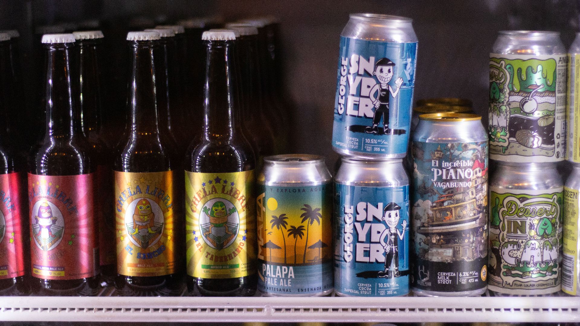 A selection of craft beer bottles and cans displayed in a refrigerator, showcasing unique branding.