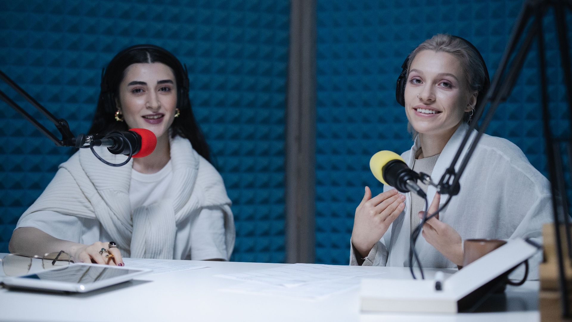 Two women podcasters engaging in discussion inside a modern recording studio with microphones.
