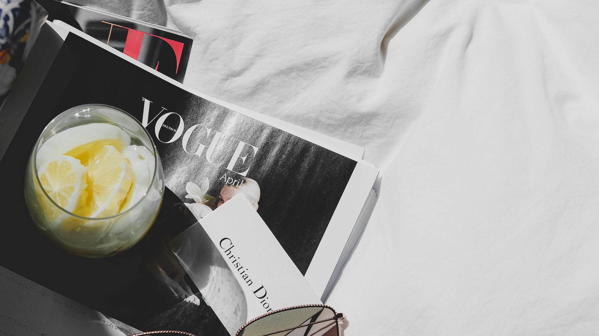 Luxurious still life featuring Dior, Vogue, sunglasses, and lemonade on white fabric in Paris.
