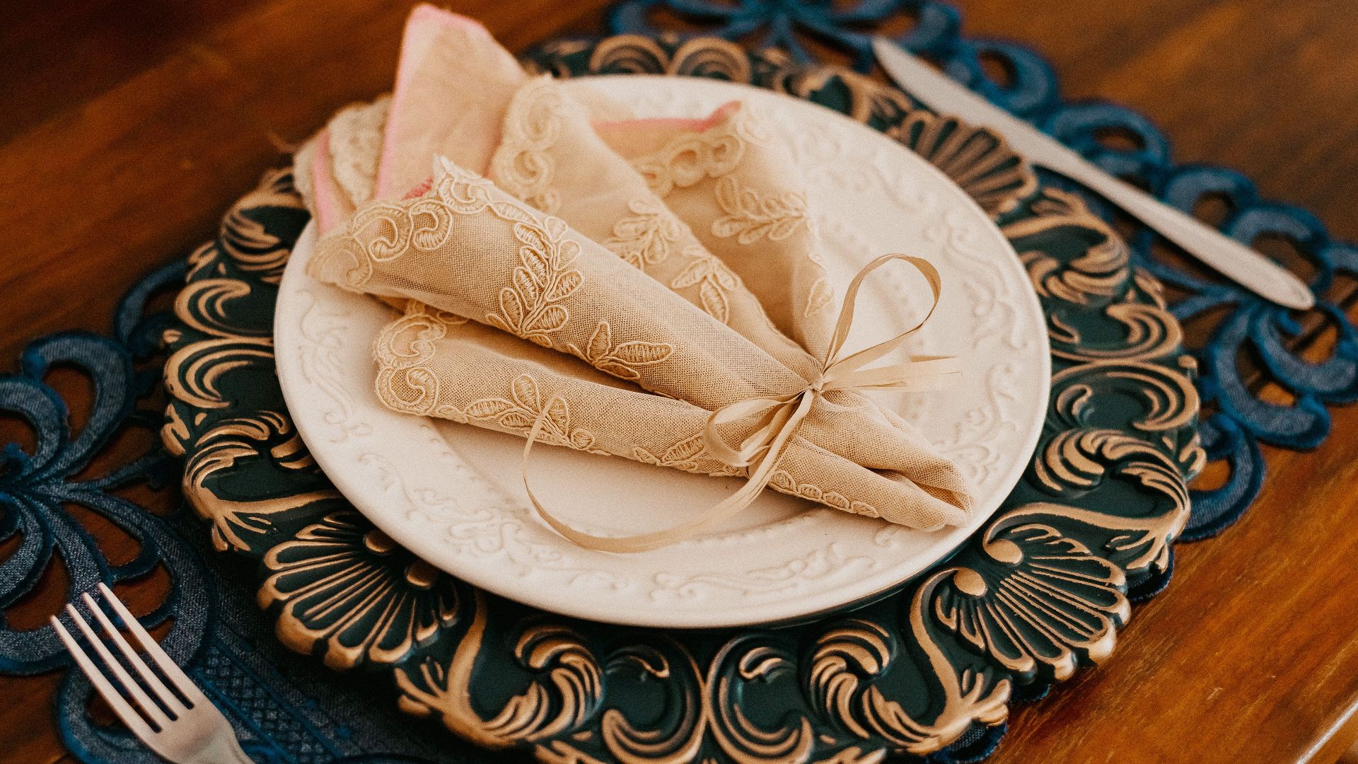 Elegant vintage table setting with embroidered napkins, plate, and cutlery on a wooden table.