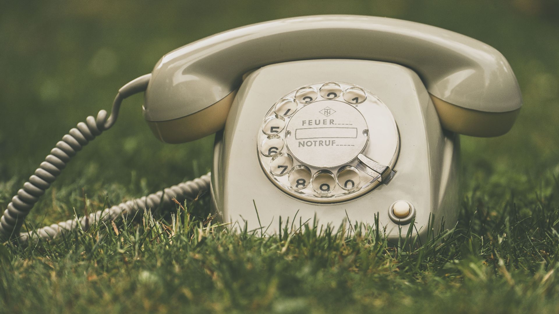 Classic rotary dial telephone placed outdoors on grass, evoking a retro feel.