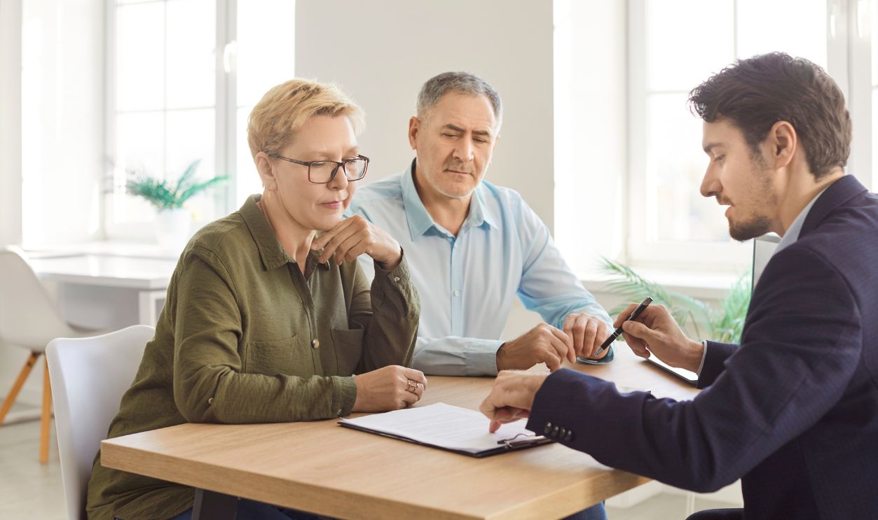 Senior couple discusses contract details with a consultant during an office meeting or negotiation. Topics include insurance, investment, and client-agent collaboration to finalize agreements.