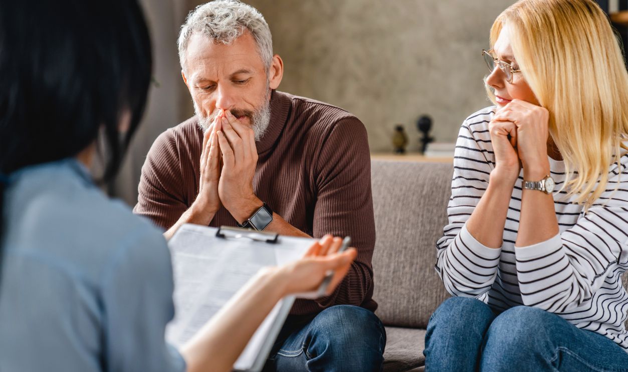 Worried middle aged couple sitting on sofa with financial advisor at home