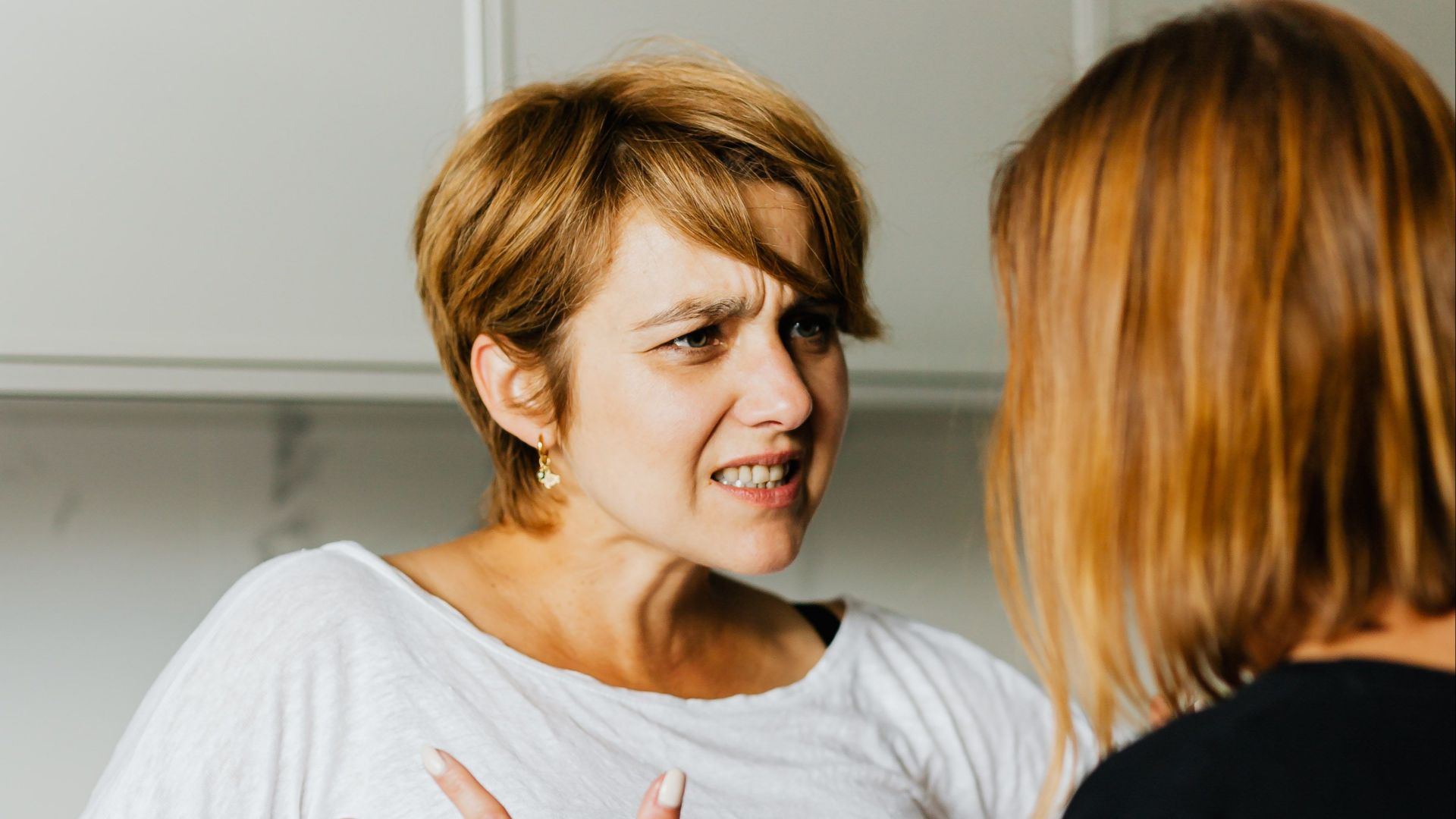 Two women engaged in a heated discussion in a modern kitchen.
