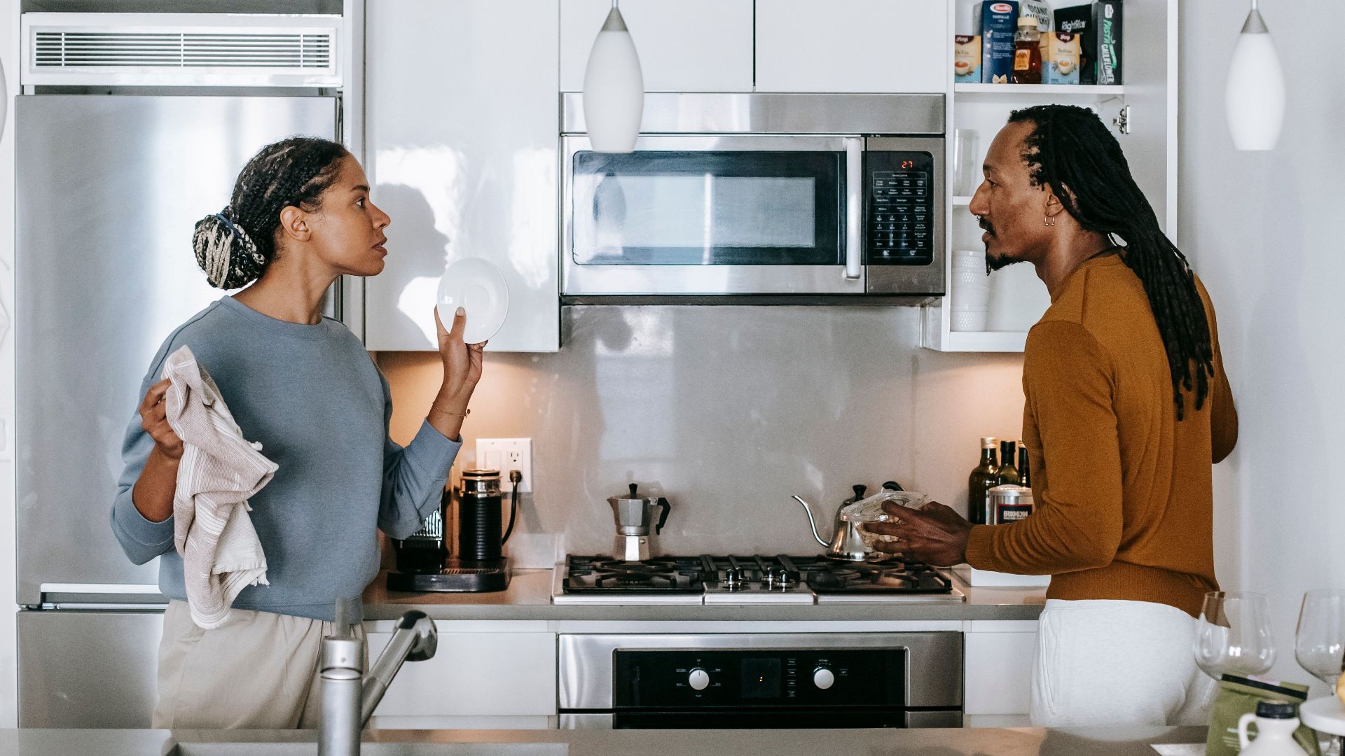 Young black woman talking to annoyed male partner while looking at each other during quarrel in house