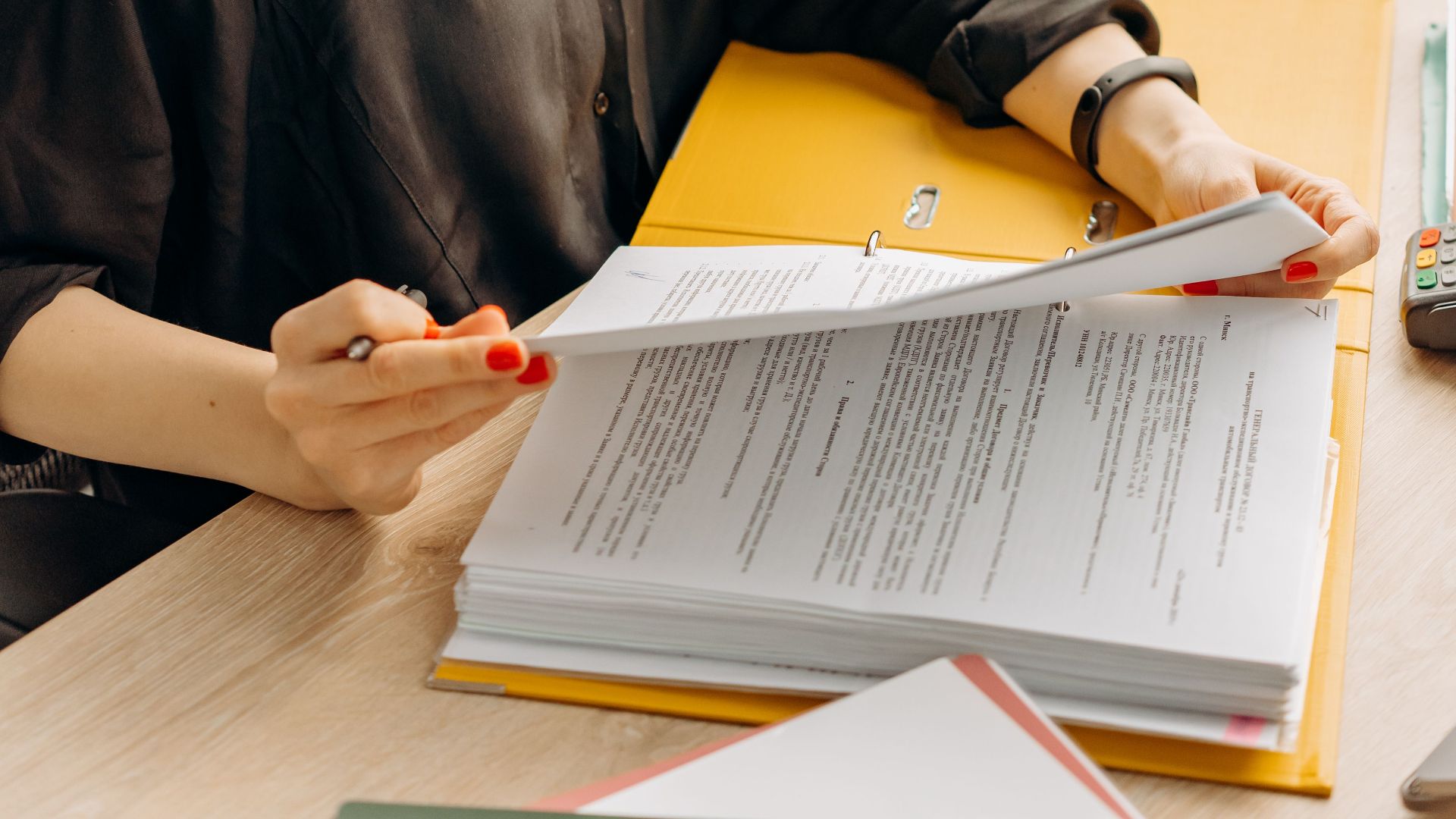 A woman in glasses sits at a desk reading documents in a modern office.