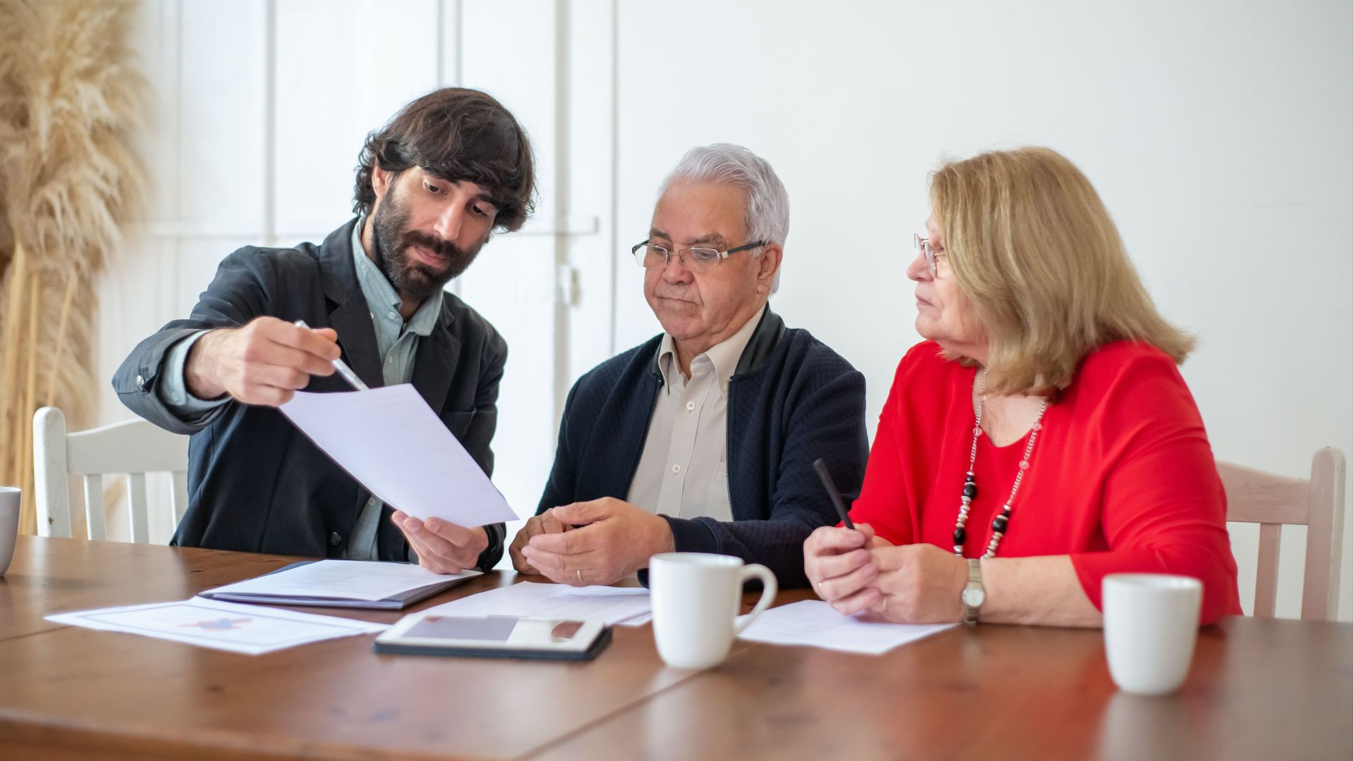 Elderly couple discussing documents with advisor at a wooden table indoors.