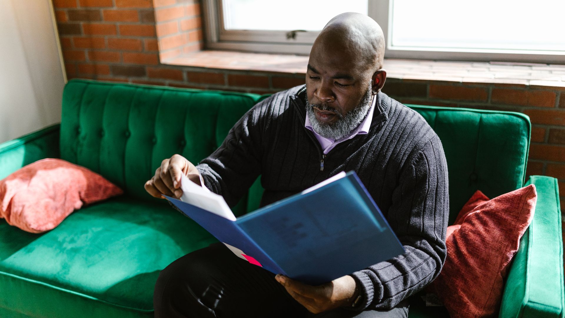 African American adult man reviewing documents on a green sofa, indoors.