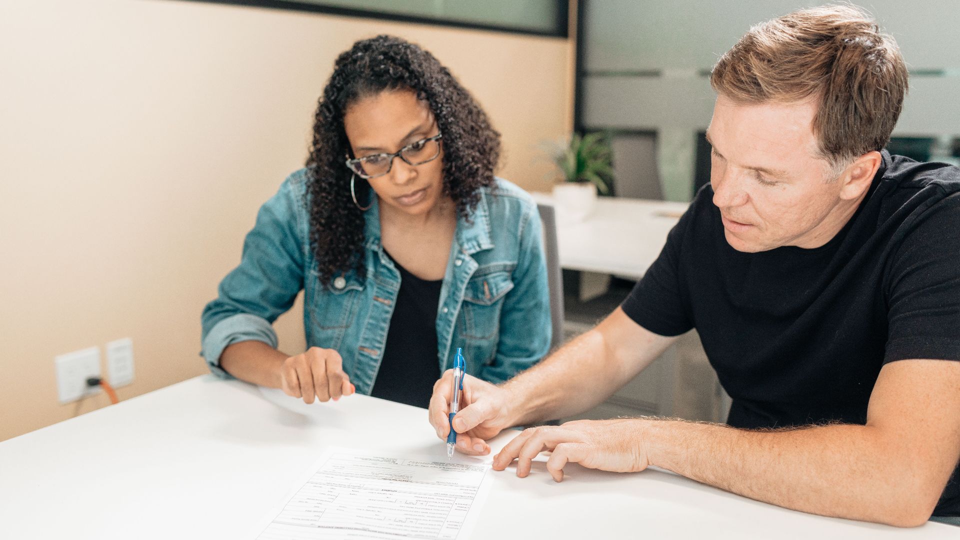 A couple working together to sign important legal documents at a desk in an office setting.