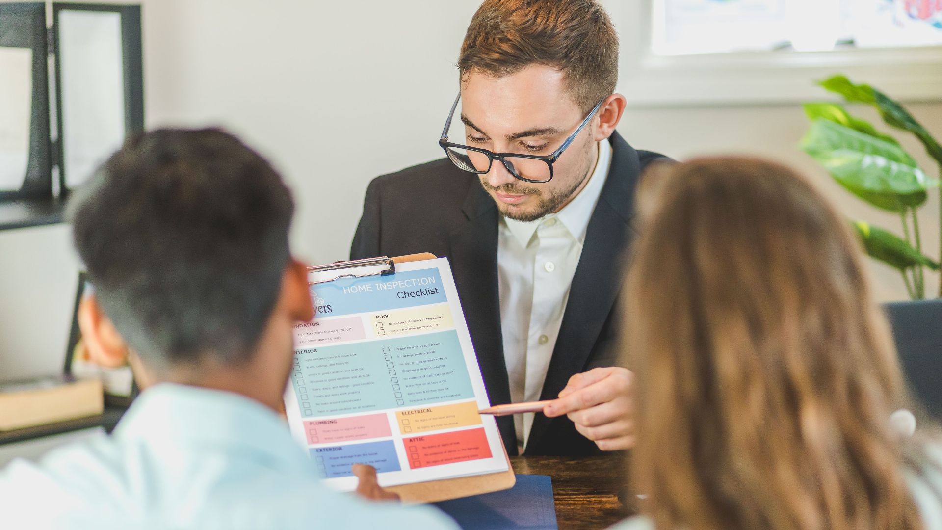 Real estate agent explaining home inspection checklist to clients in an office setting.