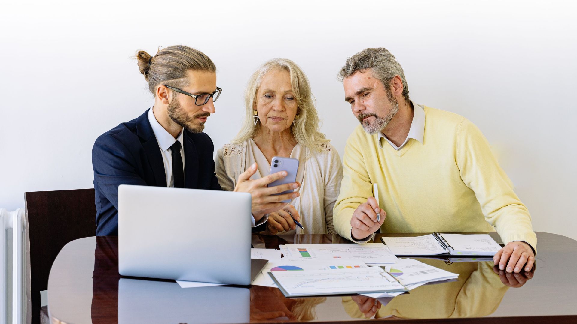 Three individuals collaborating on financial documents during a business meeting.