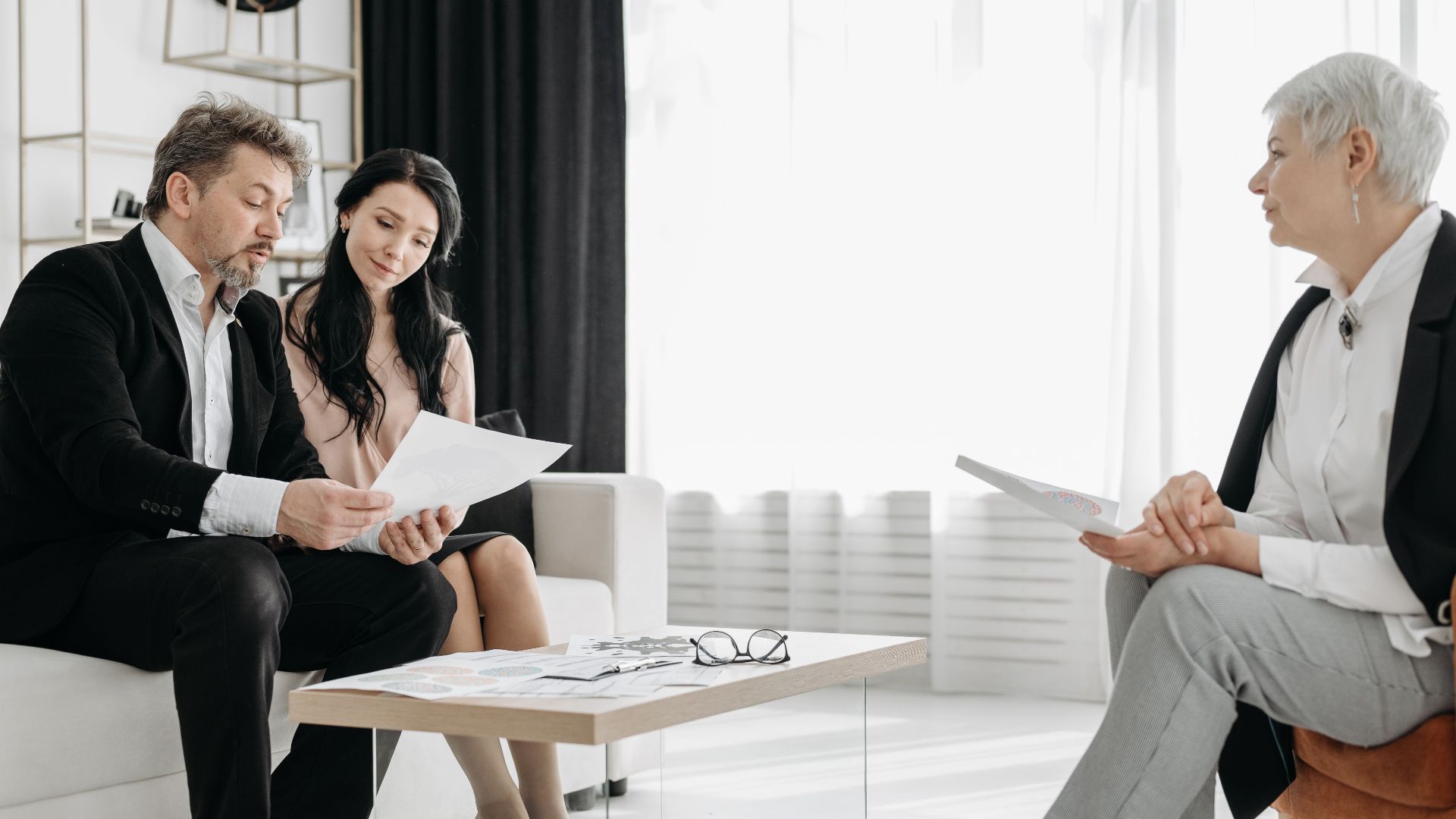 Business meeting in a modern lounge with three adults discussing documents.