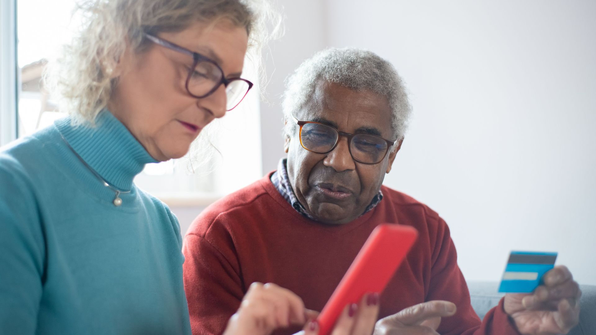 Elderly couple using smartphone and credit card for online shopping indoors.