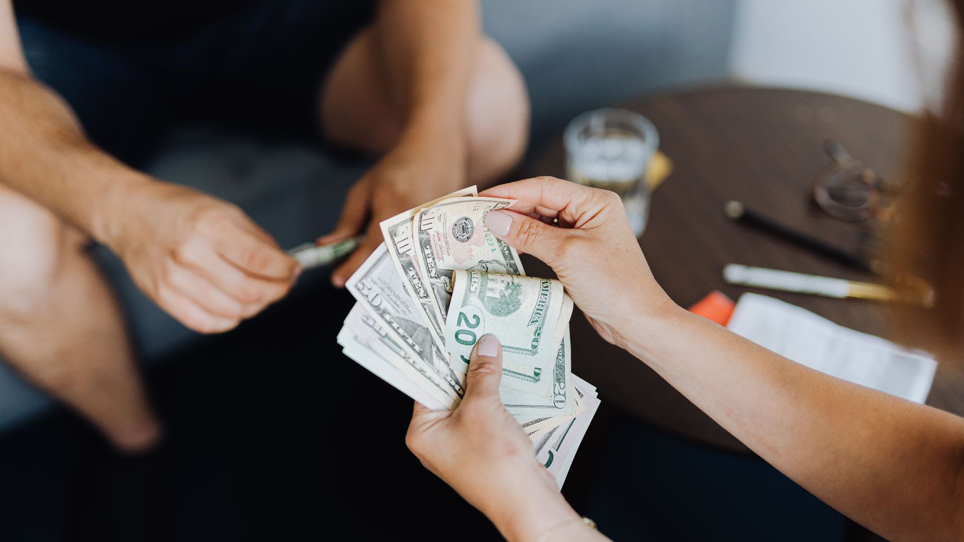 Close-up of people handling and counting US dollar bills indoors.