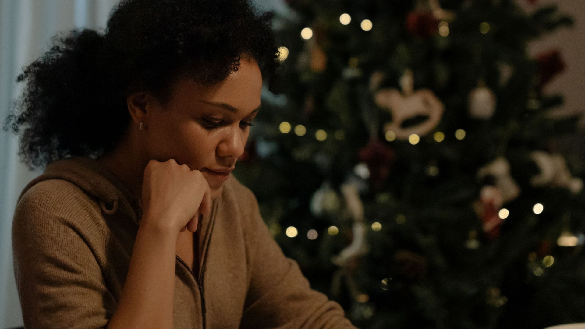 A solitary woman sitting at a dining table beside a decorated Christmas tree.