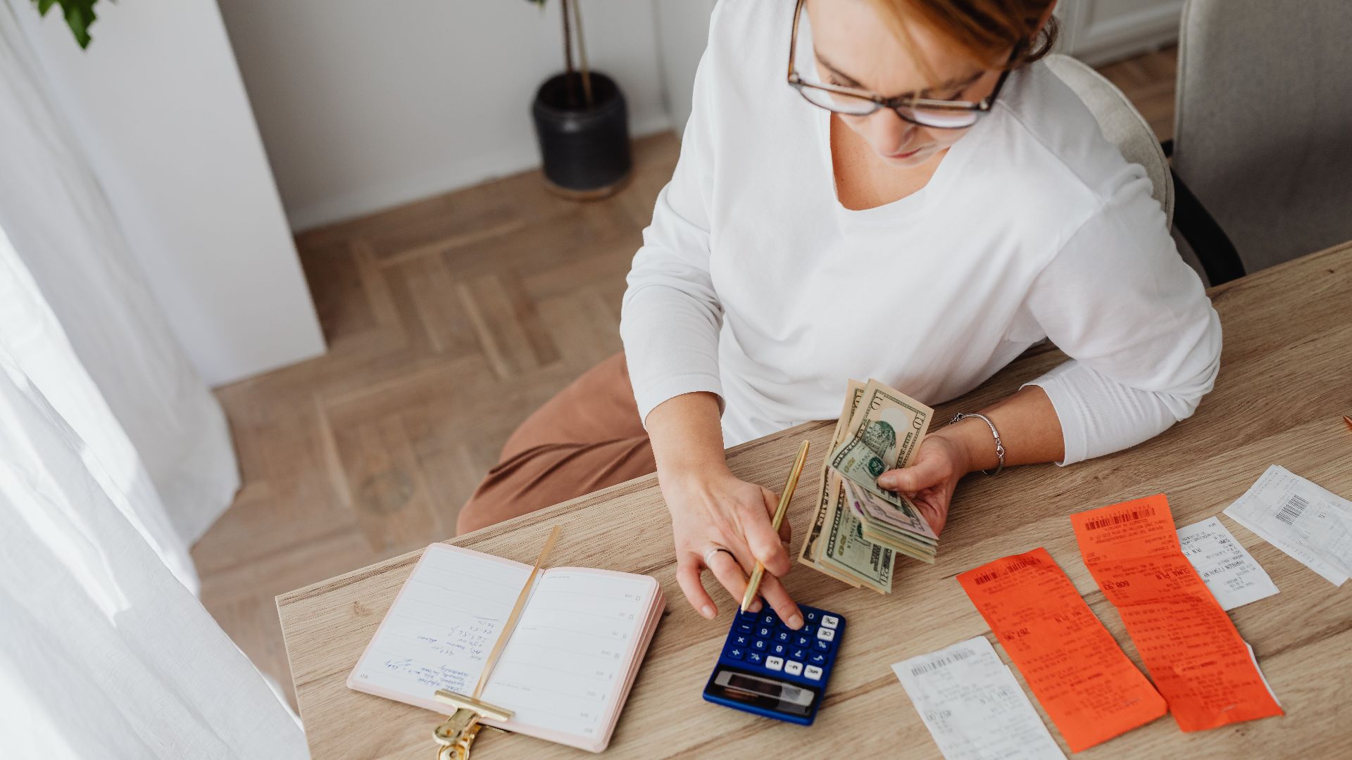 Top view of a woman managing finances with a calculator, cash, and bills in a home setting.