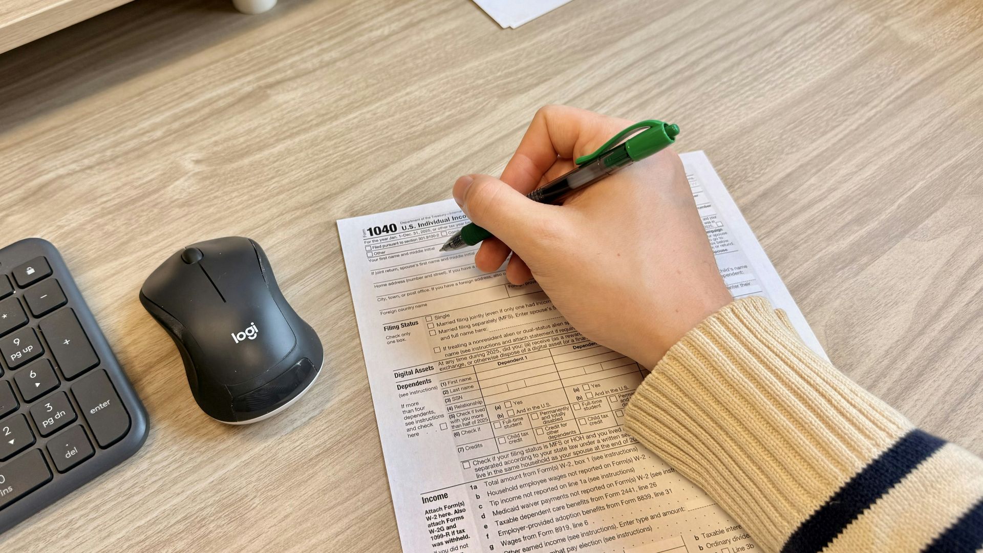 Hand writing on document next to keyboard and mouse.
