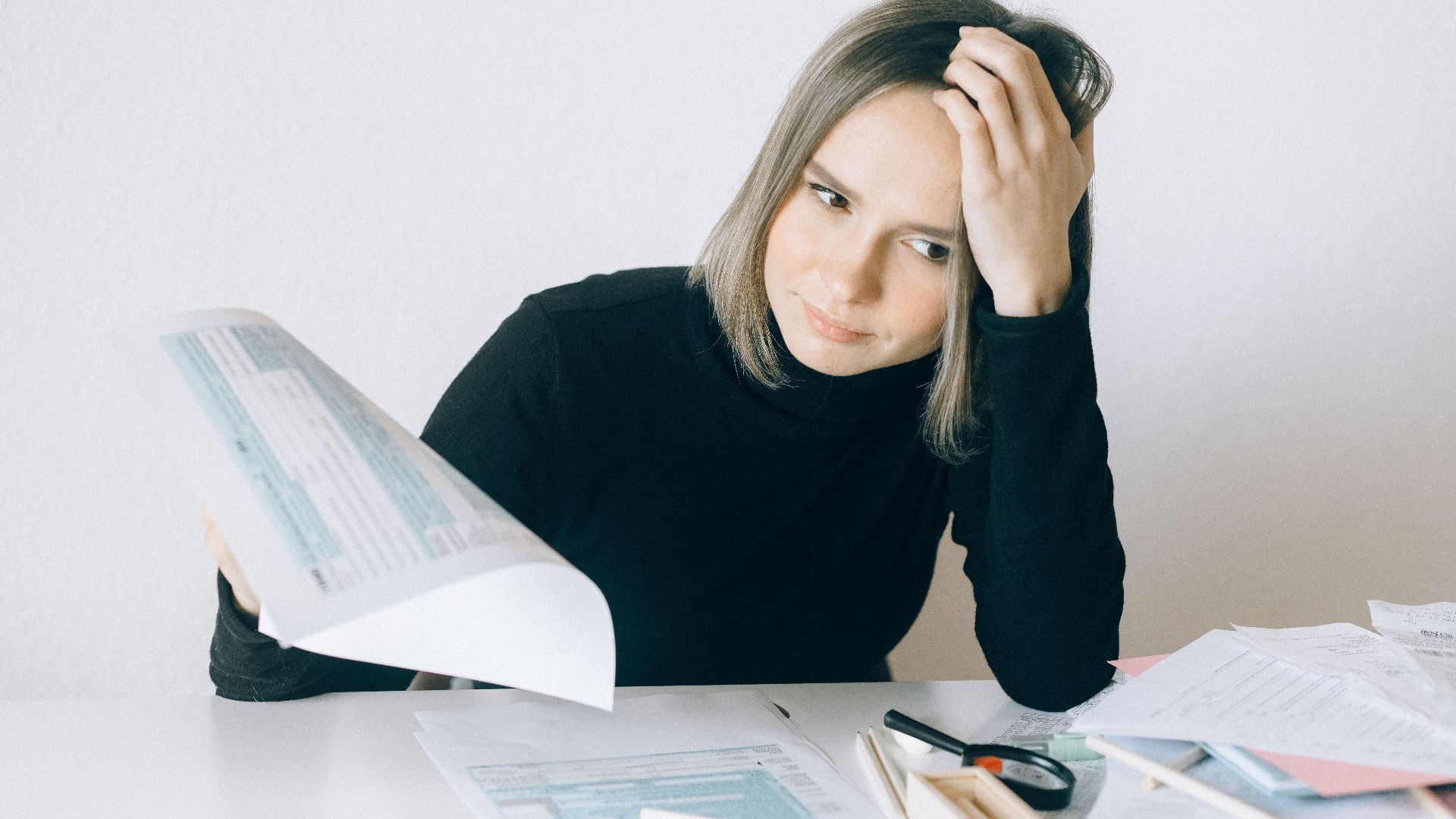 A woman showing stress while reviewing multiple paperwork and financial documents at a desk.