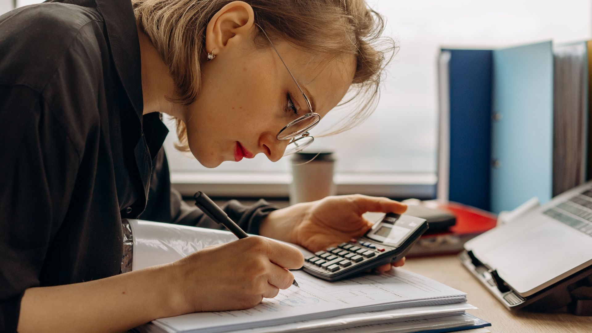 Young woman diligently working on accounting with a calculator and documents. Perfect for business and finance themes.