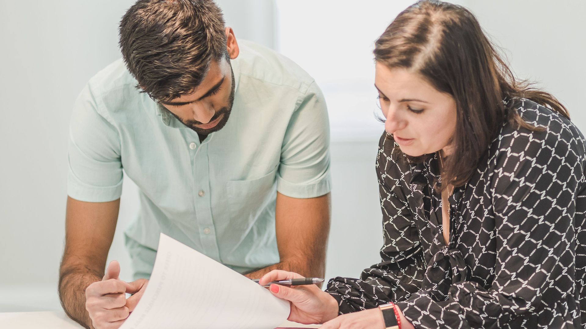 Real estate agent assisting first-time homebuyer with documents inside a bright room.